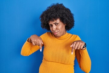 Poster - Black woman with curly hair standing over blue background pointing down looking sad and upset, indicating direction with fingers, unhappy and depressed.