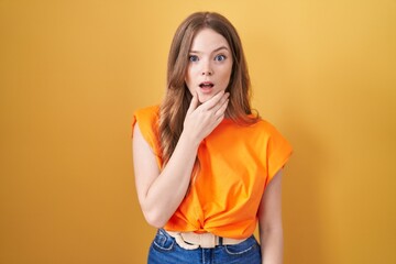 Wall Mural - Caucasian woman standing over yellow background looking fascinated with disbelief, surprise and amazed expression with hands on chin