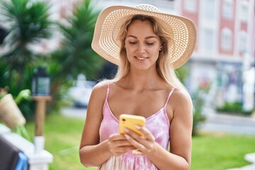 Wall Mural - Young blonde woman tourist smiling confident using smartphone at park