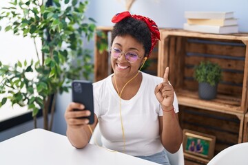 Poster - Young african american woman doing video call with smartphone smiling with an idea or question pointing finger with happy face, number one