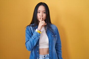 Sticker - Young asian woman standing over yellow background asking to be quiet with finger on lips. silence and secret concept.