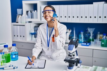 Sticker - Young african american woman scientist talking on the smartphone write on report document at laboratory