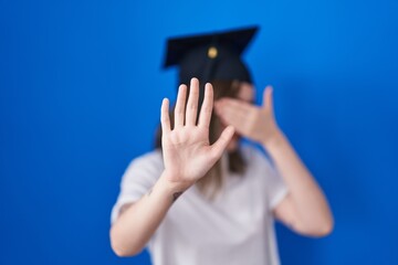 Poster - Blonde caucasian woman wearing graduation cap covering eyes with hands and doing stop gesture with sad and fear expression. embarrassed and negative concept.