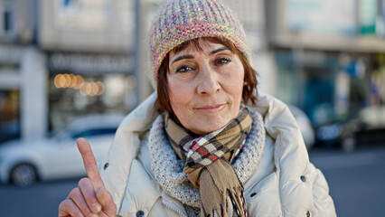 Sticker - Mature hispanic woman standing with serious expression saying no with finger at street