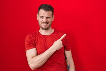 Canvas Print - Young hispanic man standing over red background pointing aside worried and nervous with forefinger, concerned and surprised expression