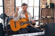 © Krakenimages.com - Young hispanic man playing classic guitar at music studio annoyed and frustrated shouting with anger, yelling crazy with anger and hand raised