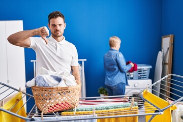 Sticker - Hispanic mother and son hanging clothes at clothesline with angry face, negative sign showing dislike with thumbs down, rejection concept