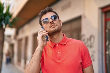 Wall Mural - Young hispanic man talking on the smartphone at street