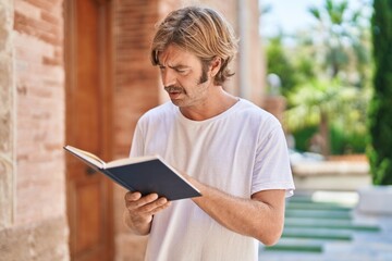 Poster - Young blond man smiling confident reading book at street