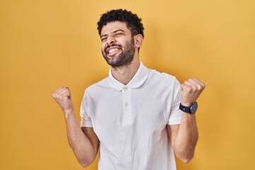 Sticker - Arab man standing over yellow background celebrating surprised and amazed for success with arms raised and eyes closed. winner concept.