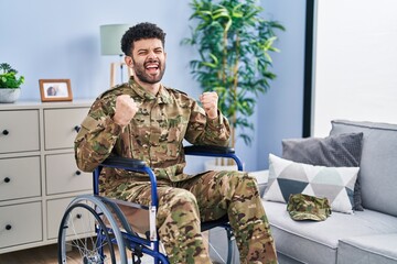 Canvas Print - Arab man wearing camouflage army uniform sitting on wheelchair very happy and excited doing winner gesture with arms raised, smiling and screaming for success. celebration concept.