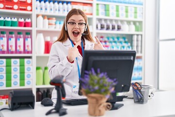 Wall Mural - Redhead woman working at pharmacy drugstore wearing headset smiling happy pointing with hand and finger