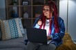 African american woman with braided hair using computer laptop at night doing money gesture with hands, asking for salary payment, millionaire business