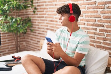 Poster - Young hispanic teenager student listening to music sitting on bed at bedroom