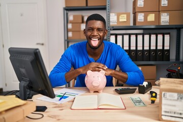 Poster - African american man working at small business ecommerce with piggy bank sticking tongue out happy with funny expression.