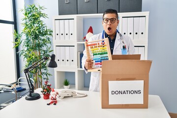 Canvas Print - Hispanic young doctor man donating toys at the clinic afraid and shocked with surprise and amazed expression, fear and excited face.