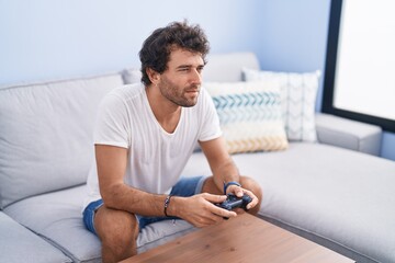 Canvas Print - Young hispanic man playing video game sitting on sofa at home