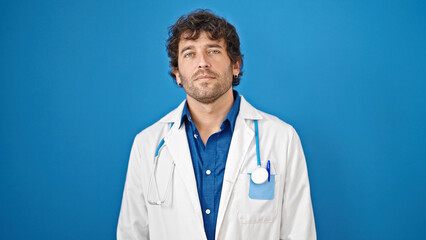 Canvas Print - Young hispanic man doctor standing with serious expression over isolated blue background