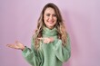 © Krakenimages.com - Young caucasian woman standing over pink background amazed and smiling to the camera while presenting with hand and pointing with finger.