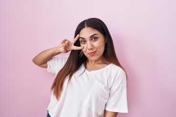 Wall Mural - Young arab woman standing over pink background doing peace symbol with fingers over face, smiling cheerful showing victory