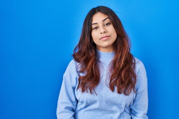 Poster - Hispanic young woman standing over blue background looking sleepy and tired, exhausted for fatigue and hangover, lazy eyes in the morning.