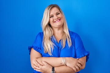 Canvas Print - Caucasian plus size woman standing over blue background happy face smiling with crossed arms looking at the camera. positive person.