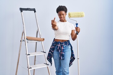 Poster - African american woman holding roller painter showing middle finger, impolite and rude fuck off expression