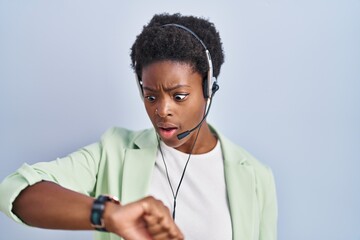 Wall Mural - African american woman wearing call center agent headset looking at the watch time worried, afraid of getting late