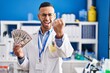 © Krakenimages.com - Young hispanic man working at scientist laboratory holding money annoyed and frustrated shouting with anger, yelling crazy with anger and hand raised