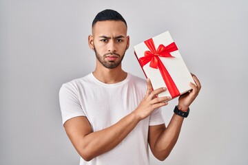 Poster - Young hispanic man holding presents skeptic and nervous, frowning upset because of problem. negative person.