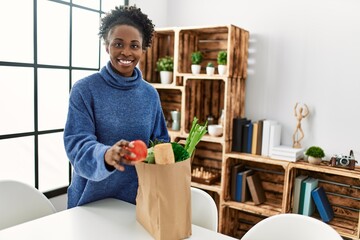 Sticker - African american woman smiling confident holding food of groceries bag at home