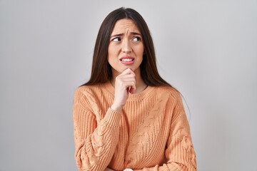 Sticker - Young brunette woman standing over white background thinking worried about a question, concerned and nervous with hand on chin