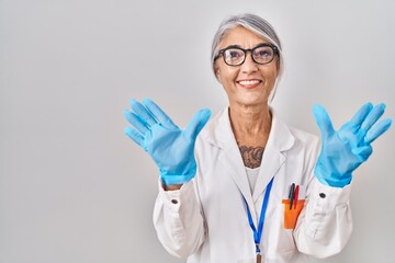 Canvas Print - Middle age woman with grey hair wearing scientist robe showing and pointing up with fingers number nine while smiling confident and happy.