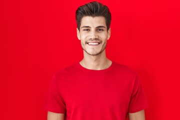 Sticker - Young hispanic man standing over red background with a happy and cool smile on face. lucky person.