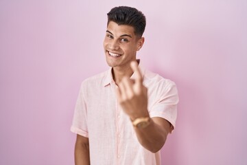 Canvas Print - Young hispanic man standing over pink background beckoning come here gesture with hand inviting welcoming happy and smiling