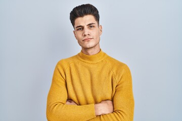 Canvas Print - Young hispanic man standing over blue background skeptic and nervous, disapproving expression on face with crossed arms. negative person.