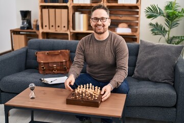 Sticker - Middle age caucasian man playing chess sitting on the sofa looking positive and happy standing and smiling with a confident smile showing teeth