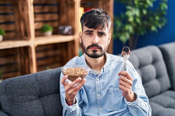 Sticker - Young hispanic man with beard eating healthy whole grain cereals relaxed with serious expression on face. simple and natural looking at the camera.