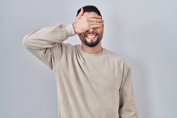 Poster - Young handsome man standing over isolated background smiling and laughing with hand on face covering eyes for surprise. blind concept.