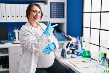 Poster - Pregnant woman working at scientist laboratory cheerful with a smile on face pointing with hand and finger up to the side with happy and natural expression