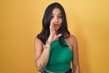 Poster - Brunette woman standing over yellow background hand on mouth telling secret rumor, whispering malicious talk conversation