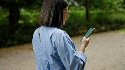 Wall Mural - Young beautiful hispanic woman using smartphone walking at the park in Vienna