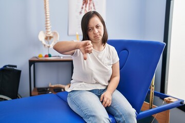 Sticker - Hispanic girl with down syndrome at physiotherapy clinic with angry face, negative sign showing dislike with thumbs down, rejection concept