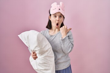 Canvas Print - Woman with down syndrome wearing sleeping mask hugging pillow surprised pointing with hand finger to the side, open mouth amazed expression.