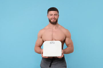 Poster - Happy athletic man holding scales on light blue background. Weight loss concept