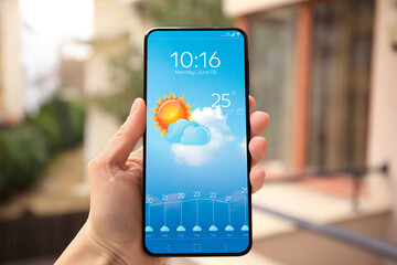 Wall Mural - woman checking weather using app on smartphone outdoors, closeup. data and illustration of sun with 