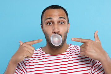 Wall Mural - Portrait of young man blowing bubble gum on light blue background