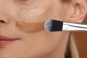 Wall Mural - Woman applying foundation on face with brush against brown background, closeup