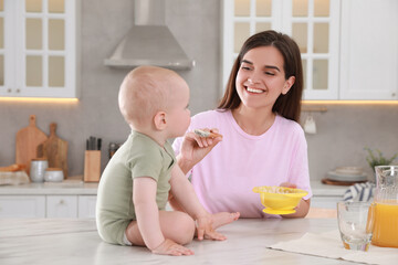 Wall Mural - Happy young woman feeding her cute little baby at table in kitchen