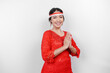 A friendly Indonesian woman is wearing red kebaya gesturing traditional greeting and Indonesia's flag headband to celebrate Indonesia Independence Day. Isolated by white background.